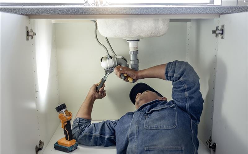 Plumber repairing pipes beneath a bathroom sink in Johnstown
