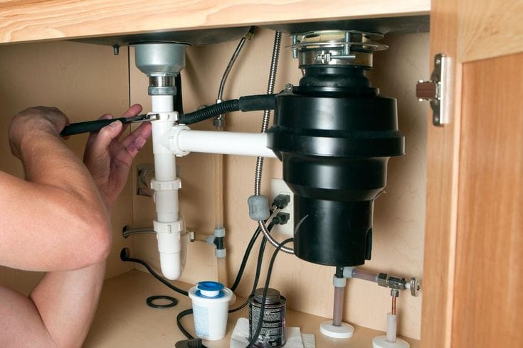 Plumber installing a garbage disposal beneath a kitchen sink in Johnstown