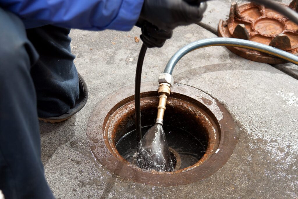 Plumber hydro jetting a sewer line through a manhole in Johnstown
