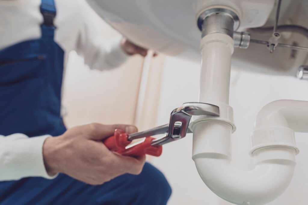 Plumber repairing a white drain pipe beneath a sink in Johnstown