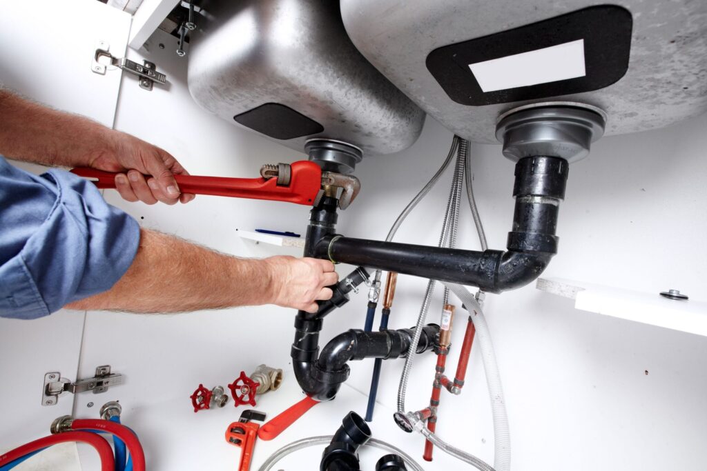 Plumber repairing drain pipes beneath a kitchen sink in Johnstown